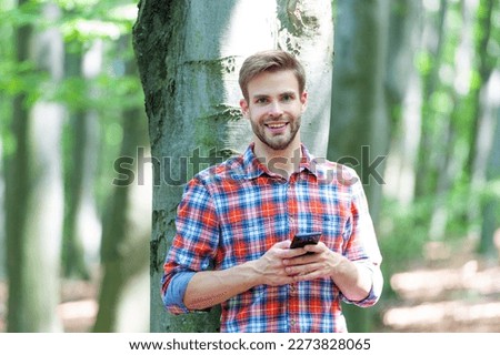 photo of happy man messaging on phone in the forest. man messaging on phone outdoor.