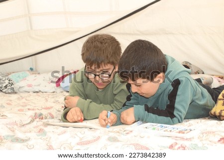 Earthquake survivor boys drawing in tent. Royalty-Free Stock Photo #2273842389