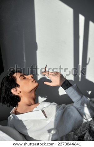 relaxed young man gets pleasure from smoking sitting on the sofa at home, close up side view shot