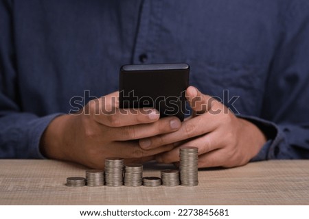 successful businessman in shirt holding mobile smartphone with stack of coins. managing investments, medical insurance payments in mobile banking application icon, personal savings expenditures.