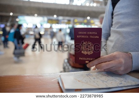 Close-up of an Italian passport held by a traveler with a map beside it. Royalty-Free Stock Photo #2273878985