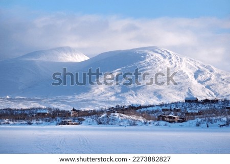 Beautiful scenery of buildings at foot of snowy mountains on coast of Lake Torneträsk (Tornestrask) around Abisko National Park (Abisko nationalpark). Sweden, Arctic Circle, Swedish Lapland