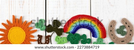St Patrick's Day concept. Knitted composition of a green hat, a horseshoe, a sun, a rainbow and green shamrocks on a white wooden background. Copy space, flat lay, banner