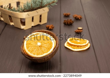 Dry slices of orange in coconut shell. Fir branch in a basket. Top view. Dark wooden background.