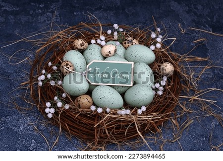 Green pastel Easter eggs and quail eggs in a nest with Easter greetings on a label. German inscription means Happy Easter.