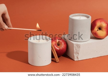 A hand lights a candle with a match stick. Aromatic soy candles in gray concrete caps with apple and cinnamon. Poster banner for candle shop, beauty, spa Royalty-Free Stock Photo #2273908435