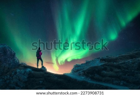 Northern lights and young woman on mountain peak at night. Aurora borealis and silhouette of alone girl on mountain trail. Landscape with polar lights. Starry sky with bright aurora. Travel background Royalty-Free Stock Photo #2273908731