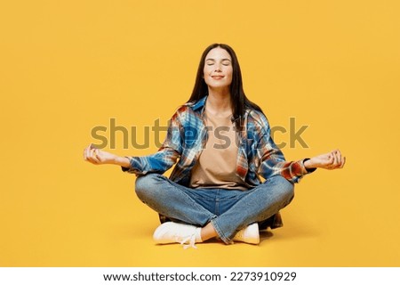 Full body young woman wears blue shirt beige t-shirt hold spreading hands in yoga om aum gesture relax meditate try to calm down isolated on plain yellow background studio. People lifestyle concept