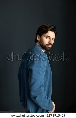 Rare view studio portrait of brutal charming bearded male model in blue cardigan wearing new men collection of warm stylish clothes, turning head at camera, isolated on black . Menswear Royalty-Free Stock Photo #2273915419