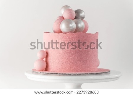Birthday cake with pink velvet sprayed coating decorated with silver and pink chocolate spheres on the white background
