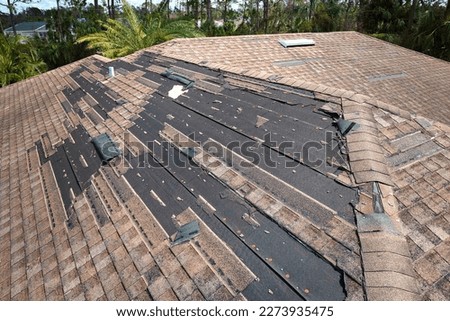 Wind damaged house roof with missing asphalt shingles after hurricane Ian in Florida. Repair of home rooftop concept Royalty-Free Stock Photo #2273935475