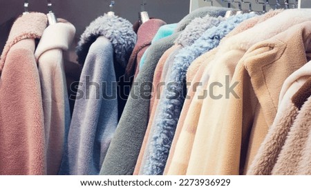 Fashion winter clothes on clothing rack - bright colorful closet. Closeup of rainbow color choice of trendy female wear on hangers in store closet or winter  fur coat