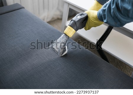 Man in protective rubber glove cleaning sofa with professionally extraction method with washing vacuum cleaner. Early spring regular cleanup. Commercial cleaning company concept Royalty-Free Stock Photo #2273937137