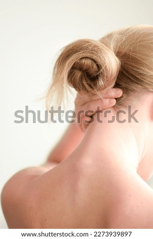 Closeup shot from back of young blonde white woman with prominent spine touching the back and having neck pain on white background. Female massaging her neck. Health care and medical concept.