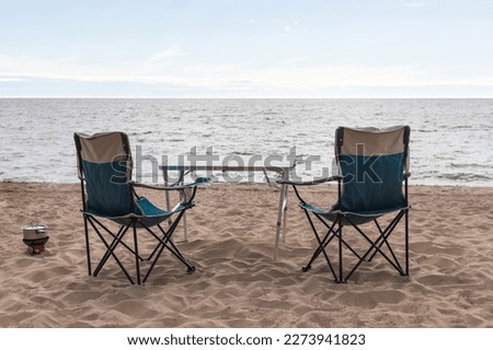 Two camp chairs and a table on the sandy shore of Lake Baikal, next on a gas burner, food is heated in a saucepan.Tourism concept Royalty-Free Stock Photo #2273941823