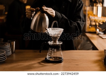 Pour over filter coffee alternative brewing method. Pouring hot water over roasted and ground coffee beans contained in paper filter Royalty-Free Stock Photo #2273942459
