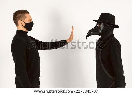 A Plague doctor and a man in a Medical mask gestures not to approach. a syringe and needle with Medicine or serum, antidote. Isolated on a white background. COVID-19, epidemic,pandemic concept.