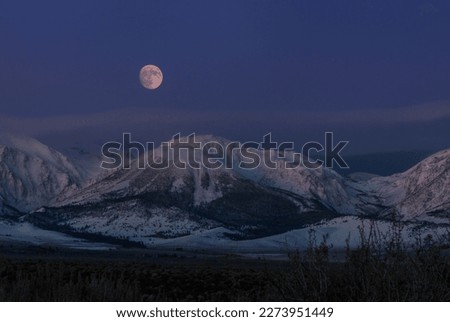 Full moon rising above snowy mountains