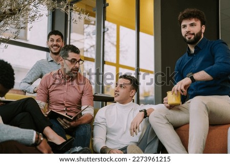 A photo of young and middle-aged colleagues having a conversation at modern office while taking a break