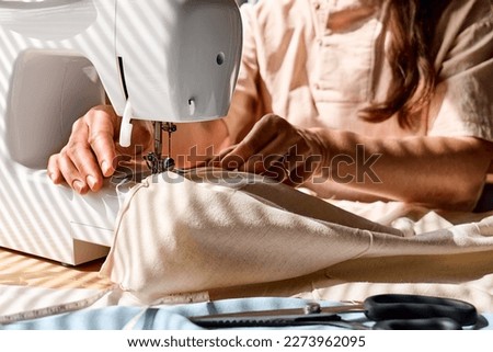 Seamstress sewing linen fabric on sewing machine in small studio. Fashion atelier, tailoring, handmade clothes concept. Slow Fashion. Conscious consumption. Royalty-Free Stock Photo #2273962095