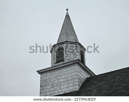 A top steeple of a church with withering paint under a cloudy sky.