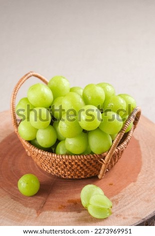 Bunch of Shine-Muscat grapes placed in the rattan basket on the wooden cutting board. White grapes. Japanese grapes. Royalty-Free Stock Photo #2273969951
