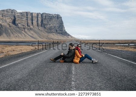 a couple sitting back to back on a lonely desert road
