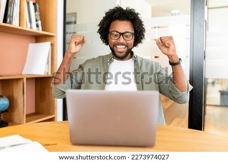 Happy excited african-american man celebrating victory sitting in the coworking in front of the laptop, lucky businessman screaming yes, receved good news, job offer Royalty-Free Stock Photo #2273974027