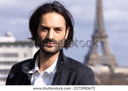Portrait of a handsome smiling young dark-haired man with the Eiffel Tower and Paris in the background
