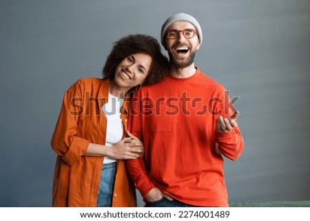 Happy stylish attractive couple of friends embracing, standing together at home. Portrait of young smiling business colleagues wearing colorful clothing looking at camera. Successful business  