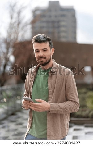 Smiling hispanic man using mobile phone, online communication standing on street. Technology concept 