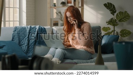Smiling ginger young business woman professional talking on phone using laptop sit at home, happy female customer make mobile call confirming online website shopping order delivery concept Royalty-Free Stock Photo #2274014599