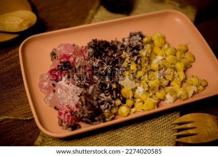 (Side of View) "cenil", sweet corn, and black sticky rice topped with grated coconut and sprinkled with sugar on a pink plate. Indonesian traditional snacks.