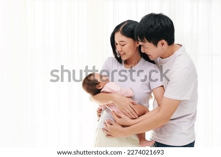 cheerful father and mother holding and hugging with newborn baby on white window background. happy family concept Royalty-Free Stock Photo #2274021693
