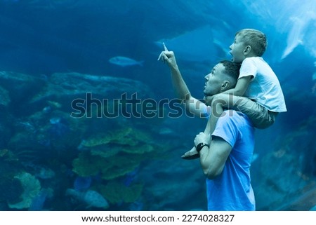 Dad and son spend time together in the Aquarium. Son sits on dad's back and explores the underwater world. Royalty-Free Stock Photo #2274028327