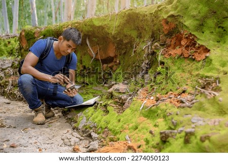 Biologist or botanist recording information about small tropical plants in forest. The concept of hiking to study and research botanical gardens by searching for information.	 Royalty-Free Stock Photo #2274050123