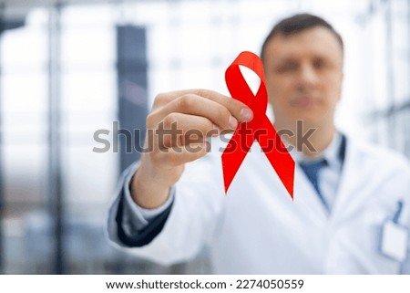 Man doctor holding a red ribbon in his hand for december world aids day, an international day of protecting people from cancer by symbol of struggle and survival mankind, for december world aids day.