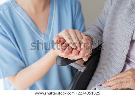 Senior woman in wheelchair indoors with Female Healthcare Professional Hand