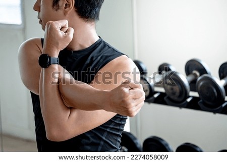 Asian sport man in black sportswear stretching arms with cross-body shoulder stretch pose and warming up before weight training in fitness gym. Physical exercise posture for muscle stretching. Royalty-Free Stock Photo #2274058009