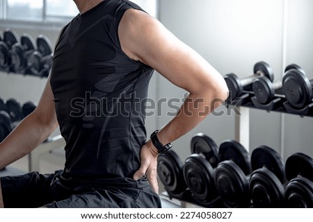 Sport man feeling lower back pain or spine pain after doing weight training exercise in fitness gym. Male athlete suffering from sport injury symptom.
