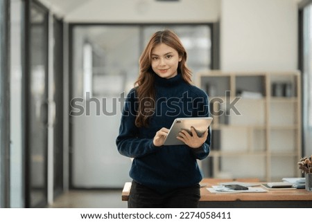 Young Asian businesswoman standing holding genuine tablet working at office Royalty-Free Stock Photo #2274058411