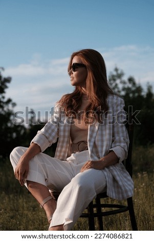 Beautiful young girl with long hair relaxing, enjoying sun sitting on chair at sunlight at summer. Backyard terrace vacation.