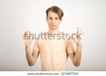 A young Caucasian blond guy with a stylish hairstyle in a yellow T-shirt shows an okay gesture isolated on a white studio background.
