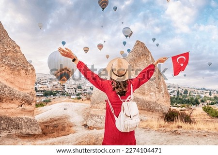 Take in the breathtaking views of Cappadocia, Turkey with a young woman as she watches the iconic hot air balloons and proudly displays the Turkish flag.