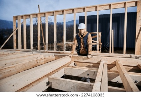 Male developer building wooden frame house. Portrait of man standing on construction site in safety helmet, inspecting quality of work. Royalty-Free Stock Photo #2274108035