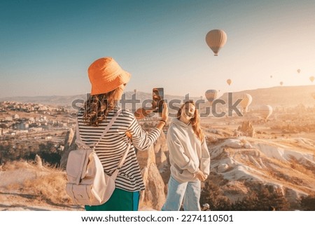 Two happy girl friends taking photos and video on phone for social networks in Cappadocia, Turkey. Travel and influencer concept