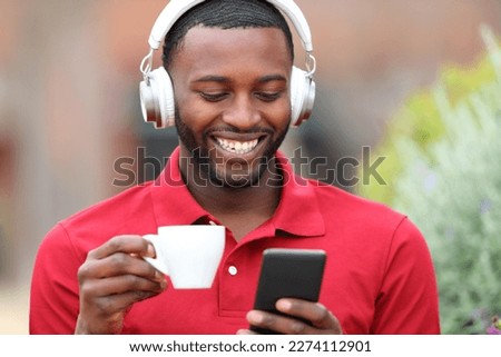 Front view portrait of a happy black man listening to music with headphones and smart phone drinking coffee