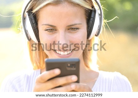 Front view of a happy teen listening to music watching phone content wearing headphone