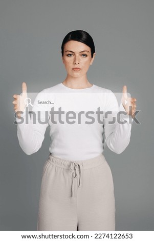 Tech-savvy woman holding a search bar icon in a studio. Young woman in her 20's recommends browsing the internet for easy access to information, as she presents the digital search field in her hands. Royalty-Free Stock Photo #2274122653