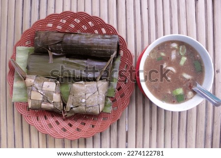 A bowl of coto makasar and a plate of lontong and ketupat on table. coto makasar is traditional soup from makasar.